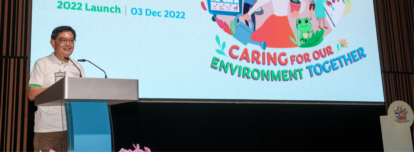Man at podium with "Clean & Green Singapore" logo; screen reads "Caring for Our Environment Together".